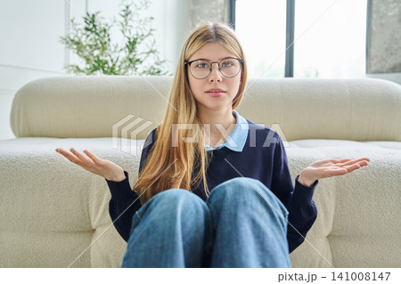 Confused teenage student girl in glasses shrugging shoulders during video call. Confused teenage student girl in glasses shrugging shoulders during video call. 141008147