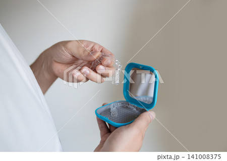 dentist holding and displaying clear aligners in a blue plastic case against a neutral background in a close-up hand-held perspective, professional and highly informative. dentist holding and displaying clear aligners in a blue plastic case against a neutral background in a close-up hand-held perspective, professional and highly informative. 141008375