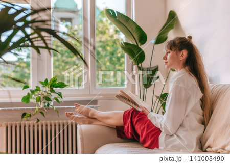Woman Sitting on Sofa Reading Book in Living Room Woman Sitting on Sofa Reading Book in Living Room 141008490