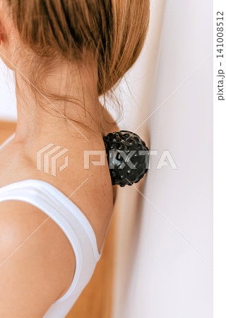 Woman Using Massage Ball on Neck Against Wall 141008512