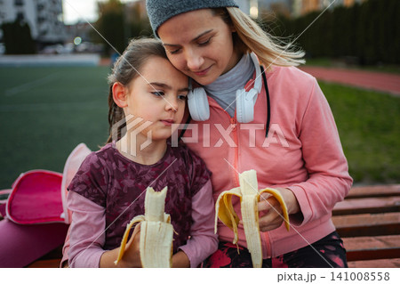 Mother and daughter bonding outdoors, eating bananas after sport Mother and daughter bonding outdoors, eating bananas after sport 141008558
