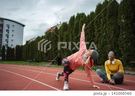 Women friends stretching on running track together Women friends stretching on running track together 141008560
