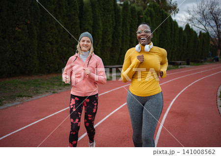 Diverse women friends running together on outdoor track Diverse women friends running together on outdoor track 141008562