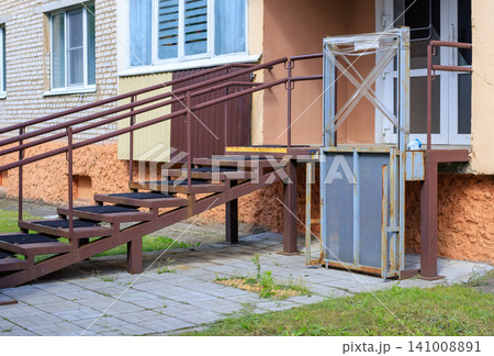Outdoor wheelchair lift next to a metal staircase at the building entrance Outdoor wheelchair lift next to a metal staircase at the building entrance 141008891