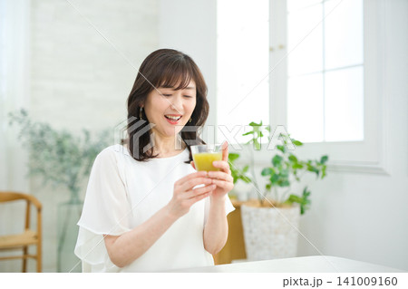 リビングで野菜ジュースを飲む60代の女性 リビングで野菜ジュースを飲む60代の女性 141009160