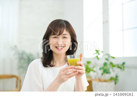 リビングで野菜ジュースを飲む60代の女性 リビングで野菜ジュースを飲む60代の女性 141009161