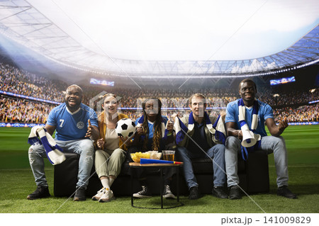 Happy soccer fans on couch cheering after goal, feeling like they are inside stadium. Cheerful football supporters together at home enjoying immersive match day during TV broadcast 141009829