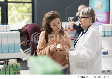 Female pharmacist advises a customer on sunscreen usage and its benefits in a modern drugstore. The healthcare worker guides the adult woman in choosing the right skincare product for her needs. Female pharmacist advises a customer on sunscreen usage and its benefits in a modern drugstore. The healthcare worker guides the adult woman in choosing the right skincare product for her needs. 141010122