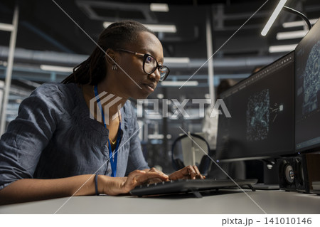 Focused server facility engineer applying AI ML tech. African American woman in server facility looking at AI programming tools on workstation check to update equipment. Focused server facility engineer applying AI ML tech. African American woman in server facility looking at AI programming tools on workstation check to update equipment. 141010146