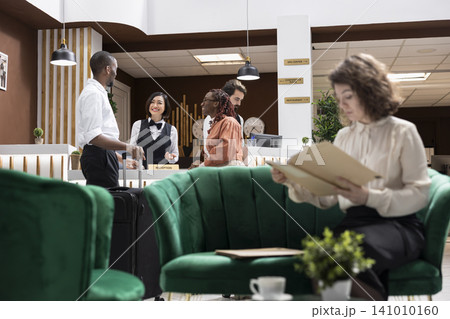Hotel concierge assisting tourists at the hotel front desk upon arrival. Asian woman staff provides reservation confirmation and registration support while guests wait in the stylish lobby. 141010160