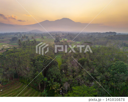 Beautiful panoramic aerial view of terraced rice fields at sunrise in Indonesia, surrounded by lush tropical greenery and palm trees. Beautiful panoramic aerial view of terraced rice fields at sunrise in Indonesia, surrounded by lush tropical greenery and palm trees. 141010878