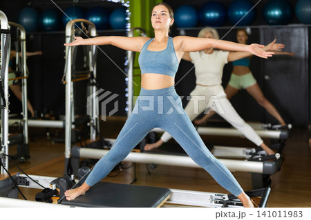 Young woman standing on pilates reformer, perform exercises 141011983