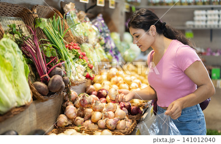 Female shopper selects onions grocery supermarket Female shopper selects onions grocery supermarket 141012040