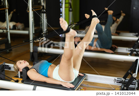 Girl lying on foldable bed reformer performs exercises, strengthening body and muscles Girl lying on foldable bed reformer performs exercises, strengthening body and muscles 141012044