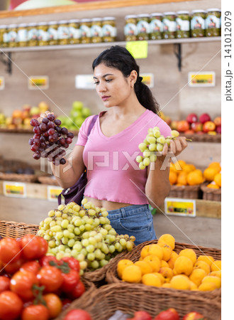Woman carefully selects ripe grape at grocery supermarket. Woman carefully selects ripe grape at grocery supermarket. 141012079