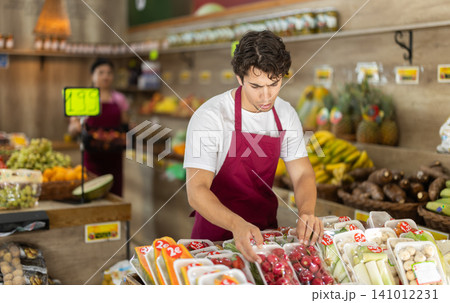 Male seller working with packaged vegetables and fruits at grocery store Male seller working with packaged vegetables and fruits at grocery store 141012231