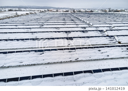 Aerial view of sustainable electrical power plant with solar photovoltaic panels covered with snow in winter for producing clean energy. Concept of low effectivity of renewable electricity in north 141012419