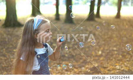 Little happy child girl blowing soap bubbles outdoors in summer park. Little happy child girl blowing soap bubbles outdoors in summer park. 141012444