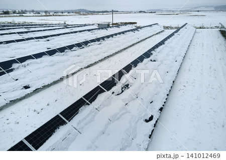 Aerial view of sustainable electrical power plant with solar photovoltaic panels covered with snow in winter for producing clean energy. Concept of low effectivity of renewable electricity in north 141012469