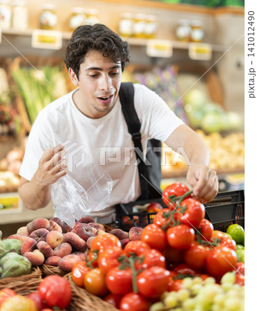 Man buys ripe tomatoes in a supermarket. European woman stands near a vegetable counter and holds tomatoes in her hands, examines them and chooses them to cook dinner 141012490