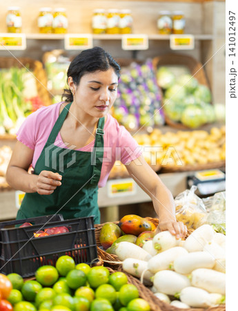 Female salesperson packages turnip on supermarket display case. Female salesperson packages turnip on supermarket display case. 141012497