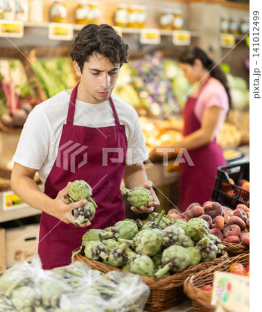 Man worker seller in grocery vegetable shop assort fruit artichoke 141012499