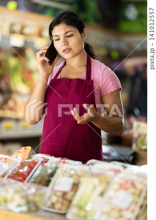 Woman seller in vegetable store is talking on phone 141012557