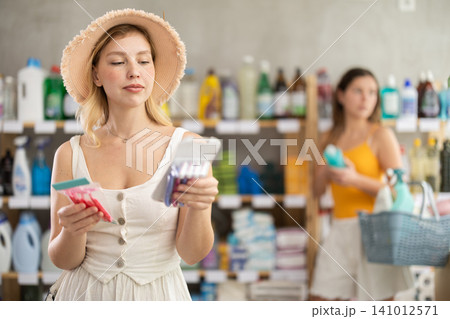 Woman consumer choose razor in household supermarket, while in background shoppers browse products Woman consumer choose razor in household supermarket, while in background shoppers browse products 141012571