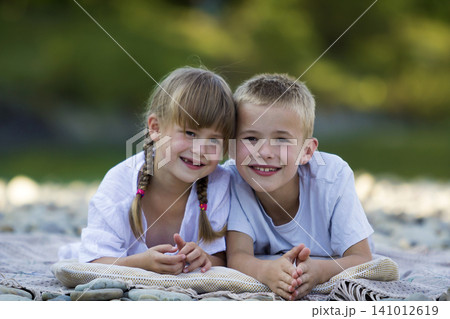 Two young happy cute blond children, boy and girl, brother and sister laying on pebbled beach on blurred bright sunny summer day background. Siblings friendship, leisure and perfect holiday concept. Two young happy cute blond children, boy and girl, brother and sister laying on pebbled beach on blurred bright sunny summer day background. Siblings friendship, leisure and perfect holiday concept. 141012619
