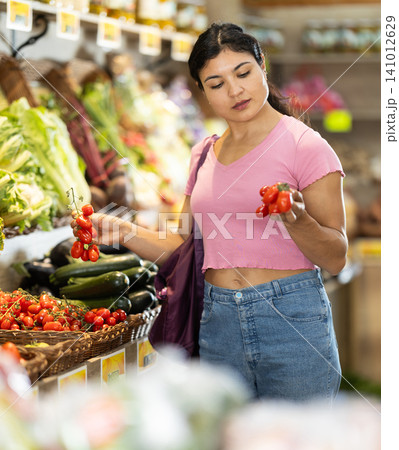 Adult woman chooses tomatoes in store Adult woman chooses tomatoes in store 141012629