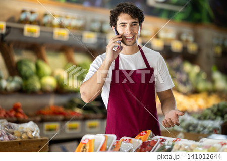 Man seller in vegetable store is talking on phone 141012644
