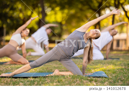Woman performing yoga asanas during group session in park 141012678