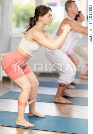 Group of women and men standing and doing stretching exercise with resistance bands in fitness studio 141012808