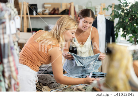 Fashionista girls near showcase examine goods, buying shorts or trousers Fashionista girls near showcase examine goods, buying shorts or trousers 141012845