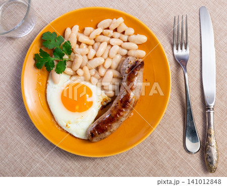 Portion of breakfast food is fried egg and pork sausage with stewed beans Portion of breakfast food is fried egg and pork sausage with stewed beans 141012848