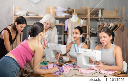 Older and younger women sewing and chatting in workroom Older and younger women sewing and chatting in workroom 141013003