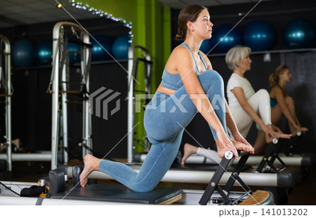Young woman standing on knee reformer, perform exercises and body tilts. Young woman standing on knee reformer, perform exercises and body tilts. 141013202