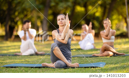 Yoga lesson visitors with coach perform Matsyendrasana in park Yoga lesson visitors with coach perform Matsyendrasana in park 141013203