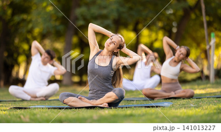 Woman performing stretches in lotus position at group yoga in park 141013227