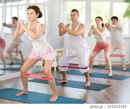Young men and women practicing half squat with band standing on mat 141013392