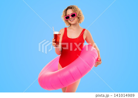 Woman holds drink, wears pink sunglasses, stands with colorful float 141014989