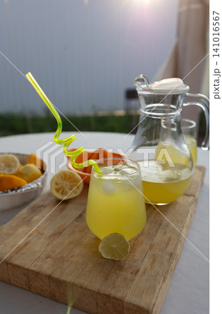 freshly served lemonade in glass with pitcher and lemons, ready to drink in outdoor setting with natural light, close-up, slightly elevated angle, vibrant yellow and green colors, mood: inv. 141016567