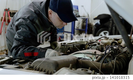 Skilled mechanic examining car engine, wearing protective gloves and performing diagnostic checks in professional workshop environment Skilled mechanic examining car engine, wearing protective gloves and performing diagnostic checks in professional workshop environment 141018315