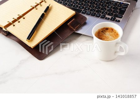 淹れたての美味しいコーヒーを飲みながら、ノートパソコンとシステム手帳でデスクワークをしているイメージ 淹れたての美味しいコーヒーを飲みながら、ノートパソコンとシステム手帳でデスクワークをしているイメージ 141018857