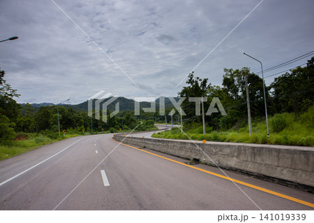 Curved empty road through green forest under cloudy sky Curved empty road through green forest under cloudy sky 141019339