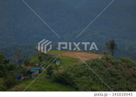 Mountain ridge landscape with grassy hilltop and distant forest under cloudy sky 141019343