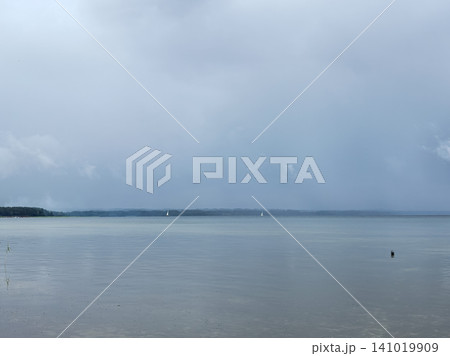 Misty lake landscape with distant sailboats under gray overcast sky 141019909