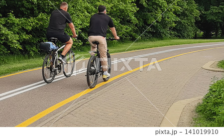 Rear view of two men on bicycles riding along a bike lane in summer Rear view of two men on bicycles riding along a bike lane in summer 141019910