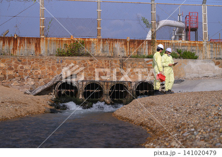 Two workers in yellow suits inspect a wastewater outfall Two workers in yellow suits inspect a wastewater outfall 141020479
