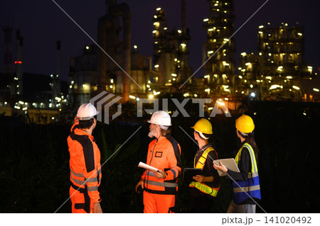Four engineers discussing inspection work outside oil refinery and petrochemical processing facility 141020492